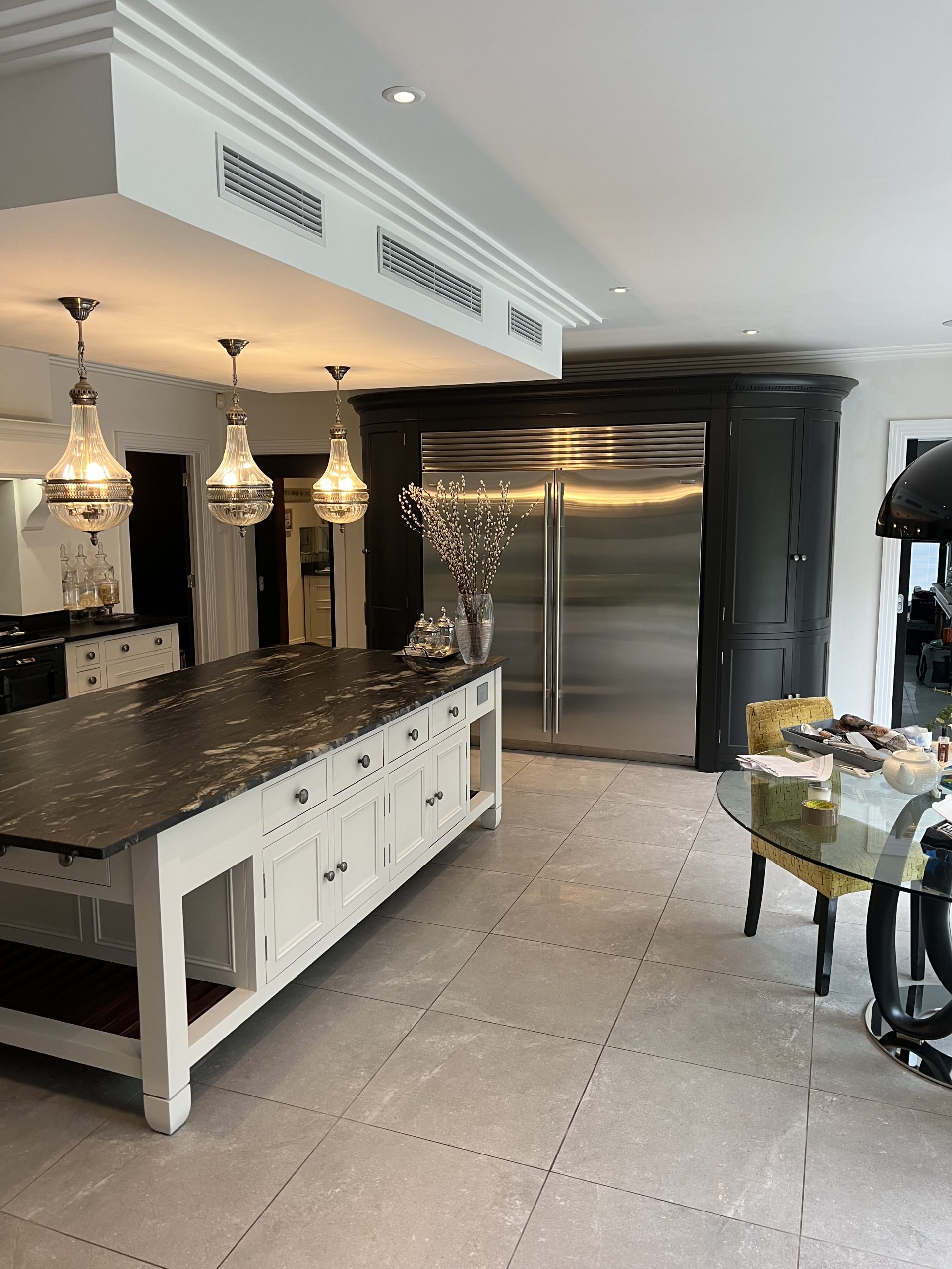 Hand-painted kitchen with a large central island, dark painted cabinetry, stone worktops and contemporary pendant lighting.