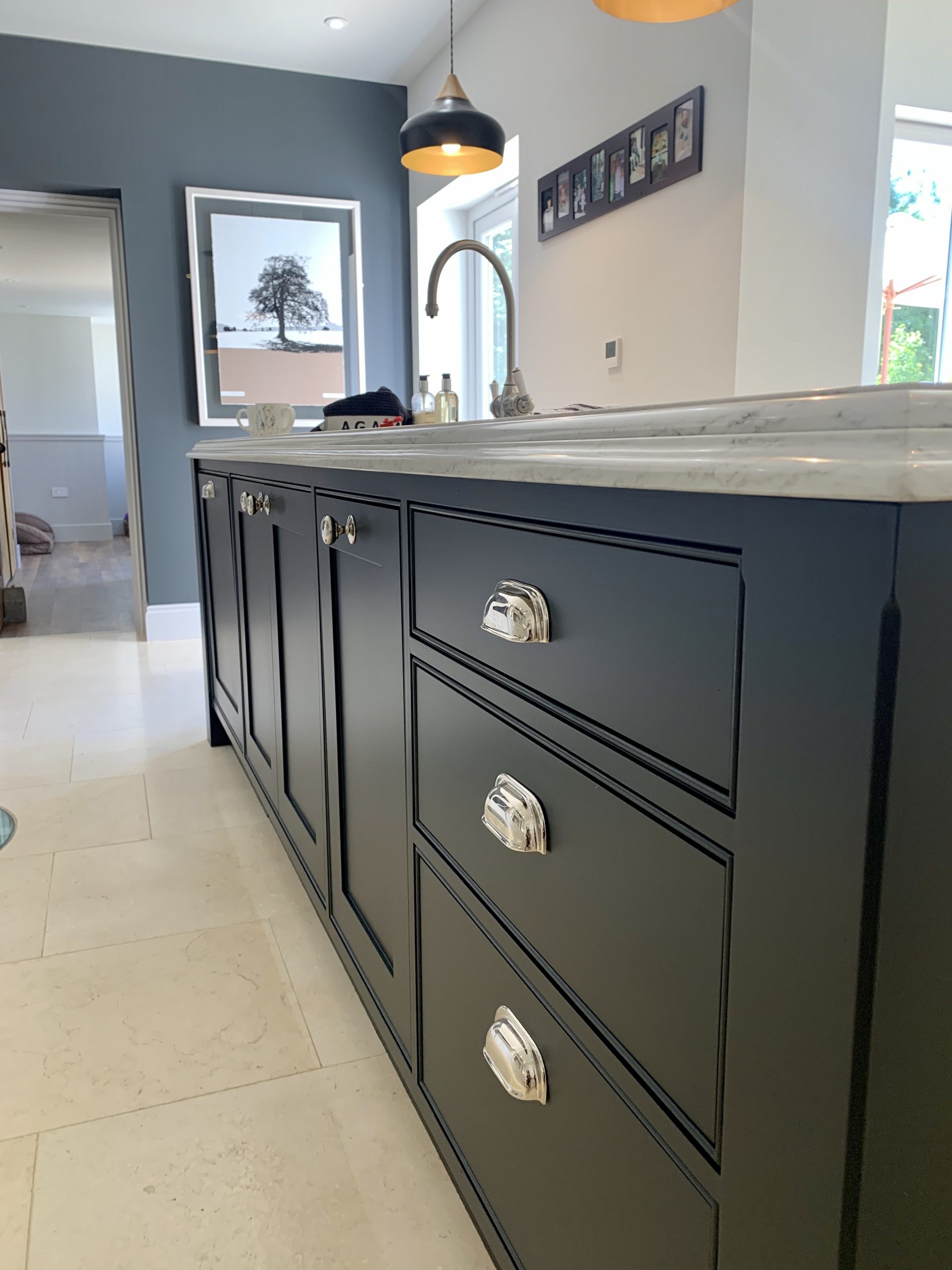 Close-up of a hand-painted navy kitchen island with shaker drawers, chrome cup handles and a stone worktop.