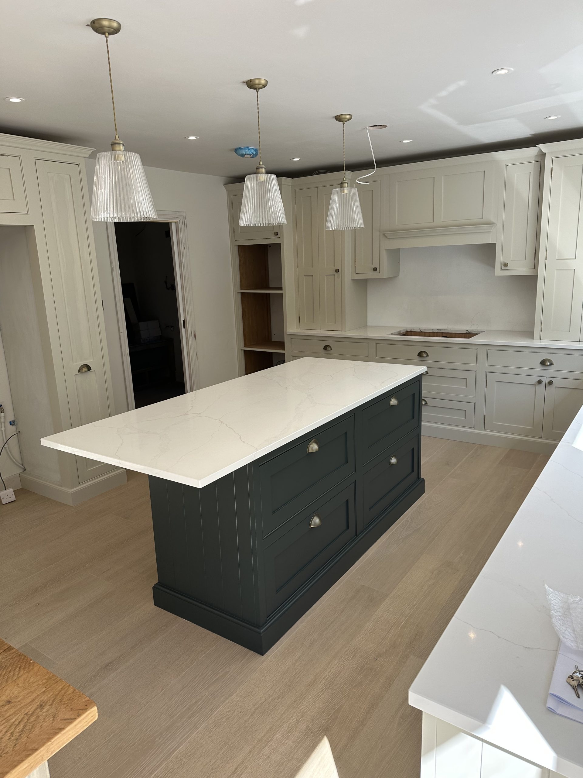 Hand-painted kitchen featuring a deep green island with white quartz worktop and off-white fitted cabinetry.