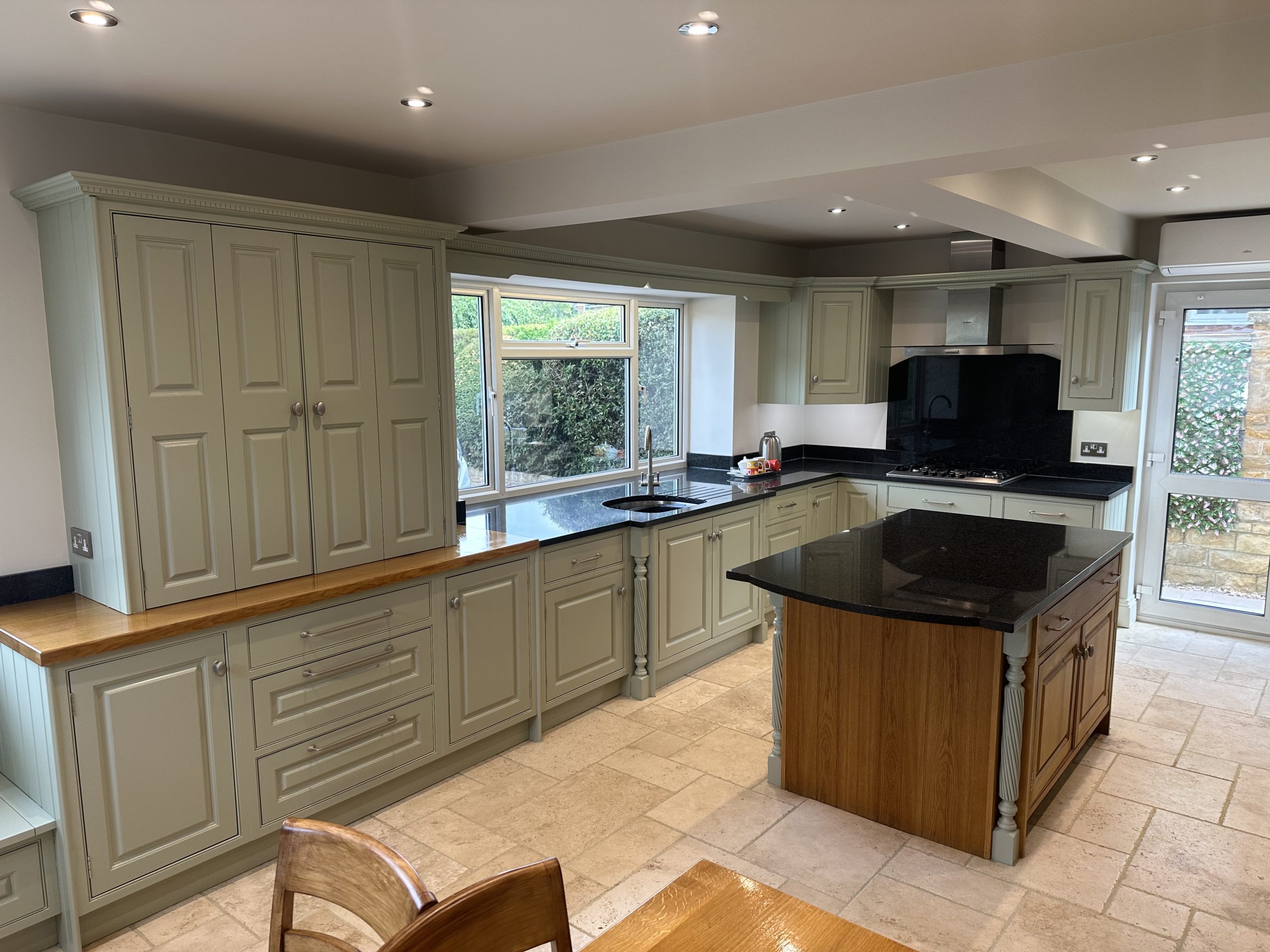 Hand-painted sage green shaker kitchen with a central island, oak worktops and bespoke fitted cabinets.