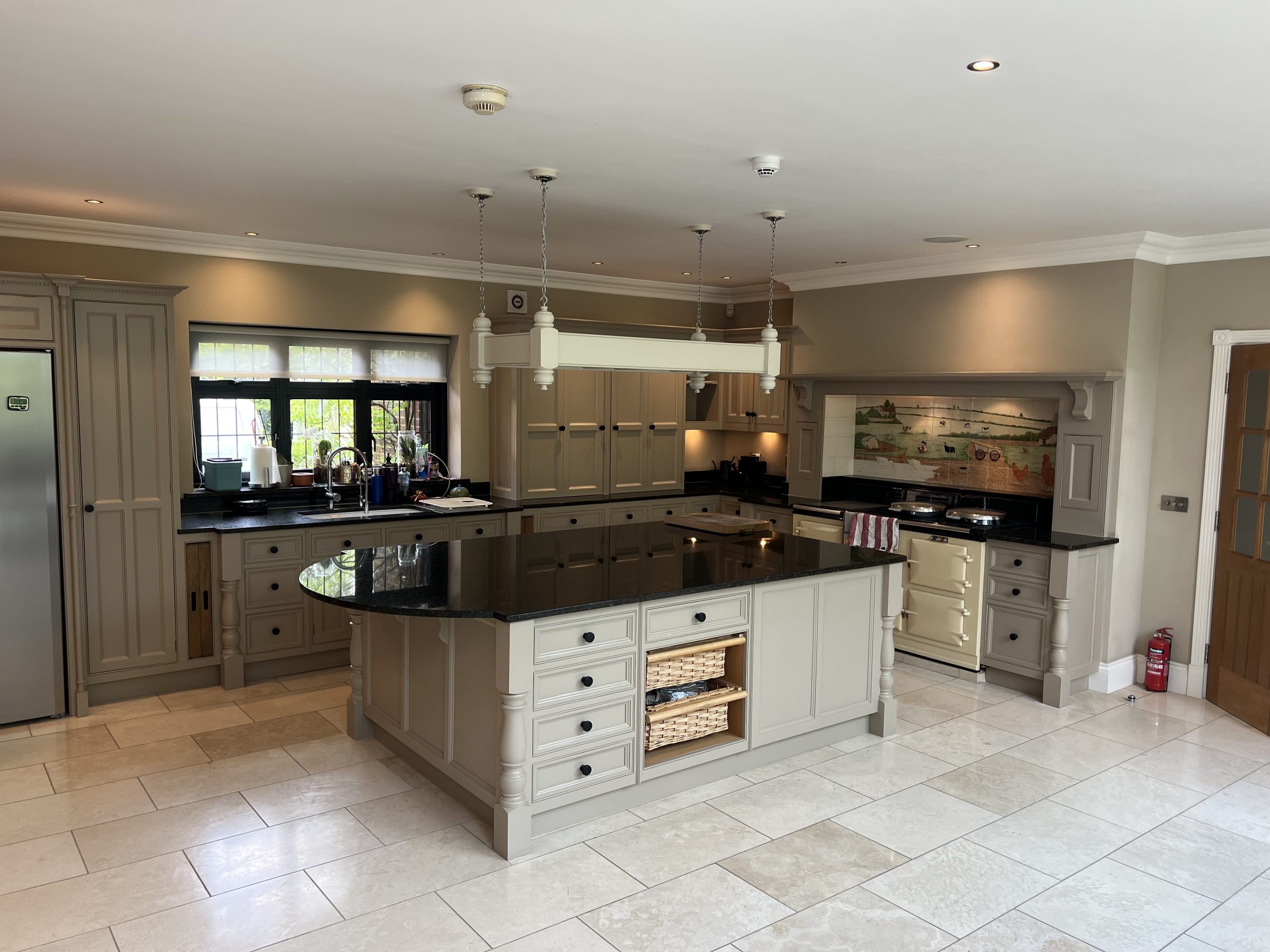 Hand-painted taupe shaker kitchen with a central island, stone flooring and bespoke fitted cabinetry.
